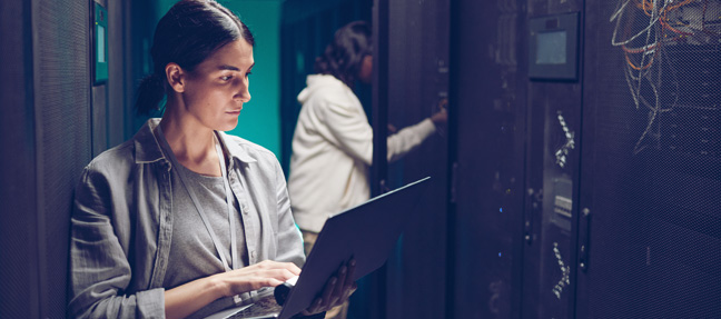 Network specialist using laptop to inspect data center infrastructure performance.