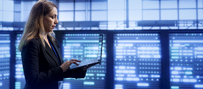 Technician analyzing network operations processes on laptop in active NOC environment